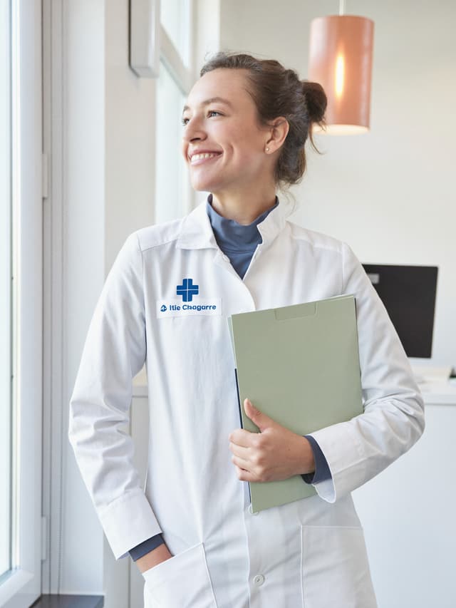 Jeune diplômée en blouse blanche regardant son badge de cabinet, entre fierté et appréhension
